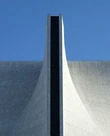 A curved concrete building facade against a blue sky, with a dark vertical seam down its centre.